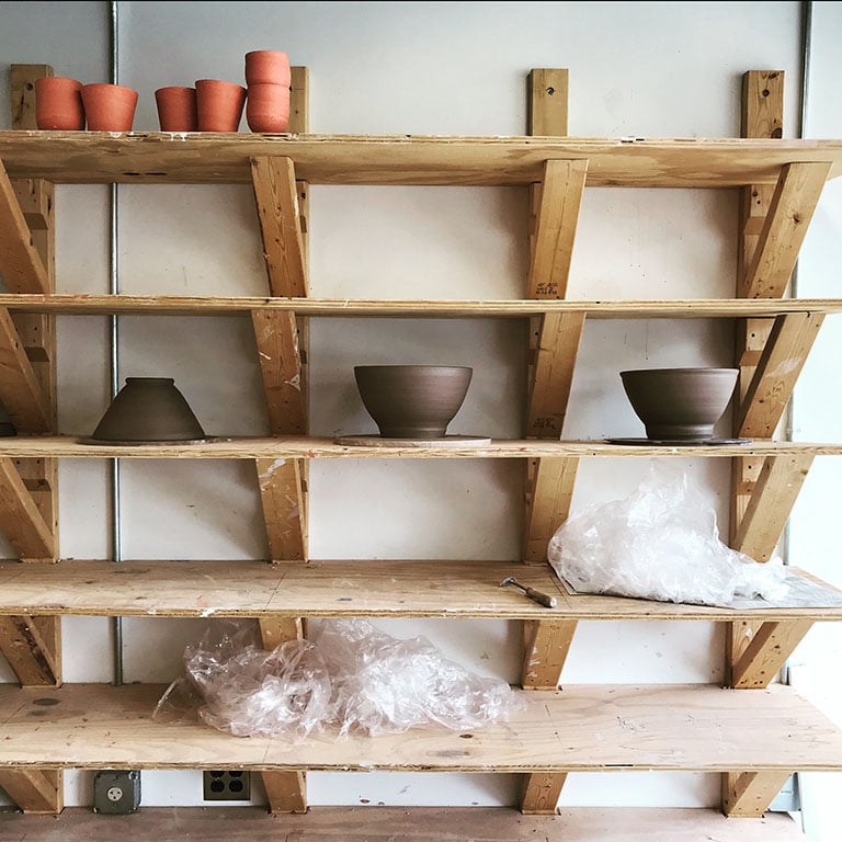 Color photo of rows of wooden shelves filled with brown clay bowls drying after being thrown on a wheel Artist megan f. hopkins eurus ceramics handmade wheelthrown pottery