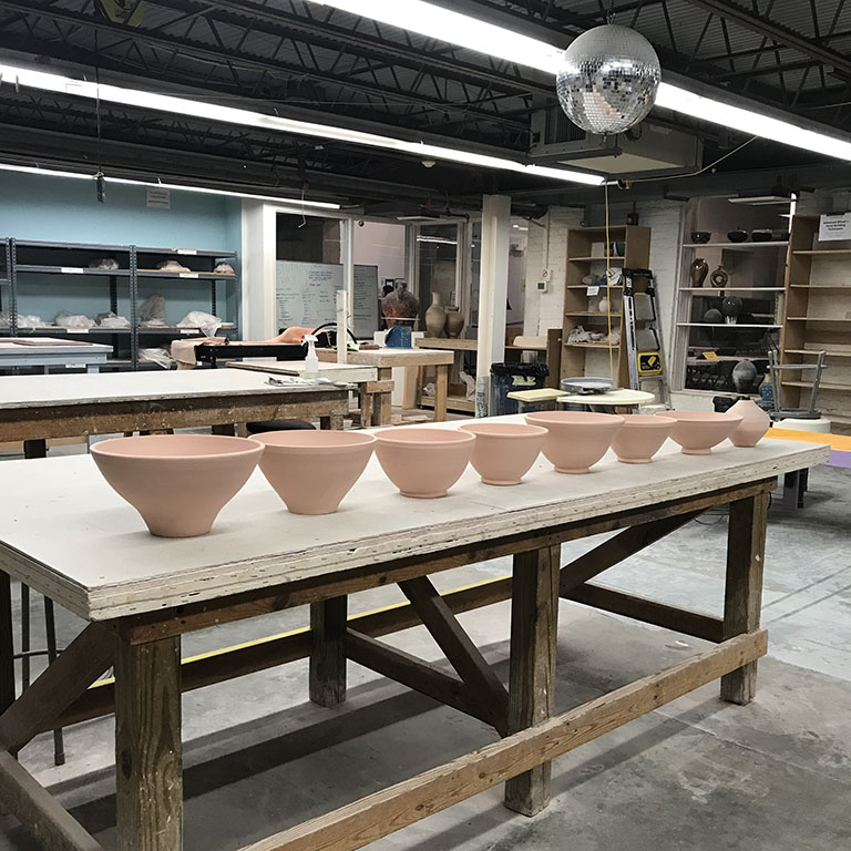 Color photo of a pottery studio table with speckled brown bisqued clay large pottery bowls lined up in a row by megan f. hopkins eurus ceramics handmade wheelthrown pottery