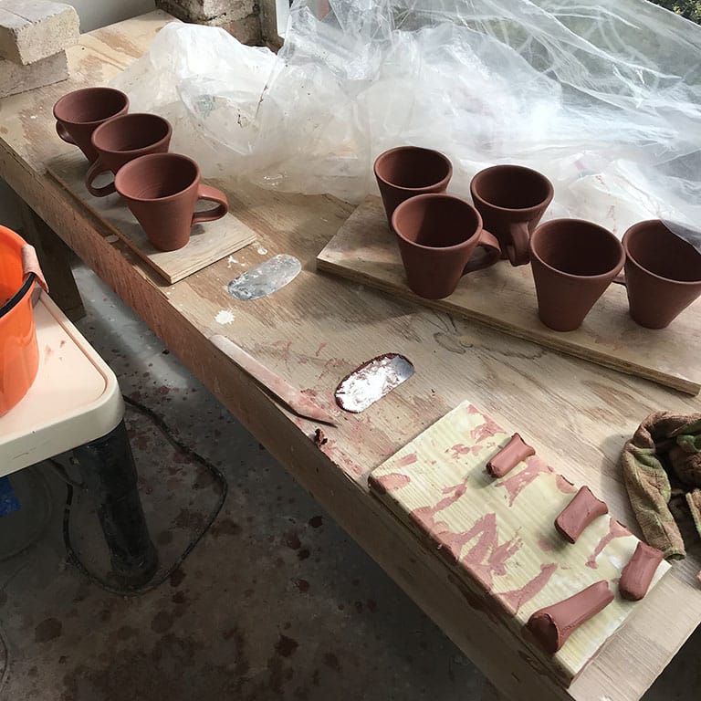 Color photo of red mugs getting handles put on in a pottery studio by megan f. hopkins eurus ceramics handmade wheelthrown pottery